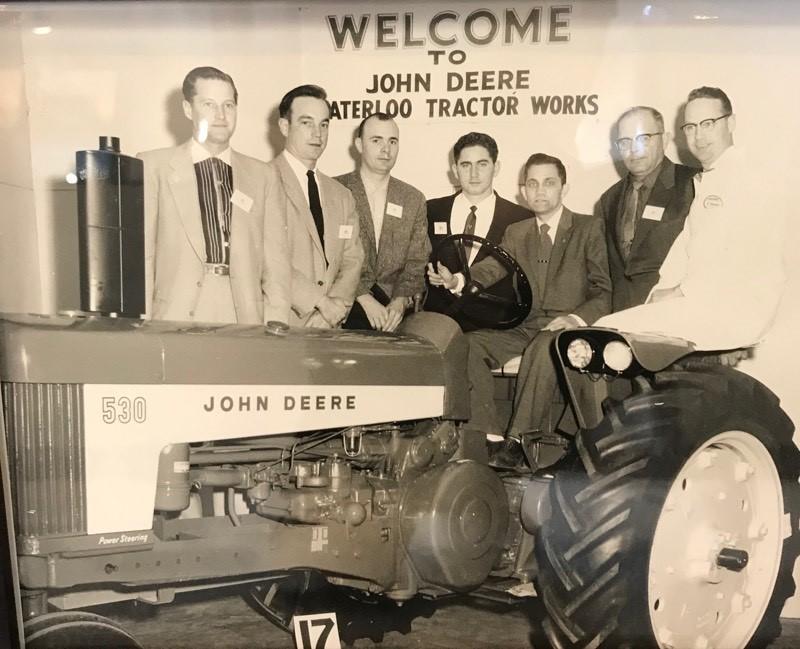 Old photo of people standing around and sitting on a john deere tractor at john deere tractor works